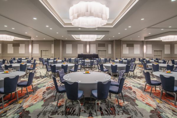 The image shows a large, elegant conference room with round tables and padded chairs arranged neatly, ready for an event, meeting, or banquet.