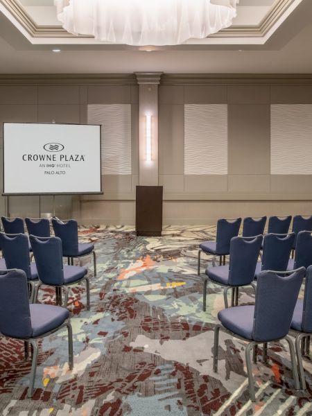 A conference room with rows of blue chairs, a podium, and a screen displaying 