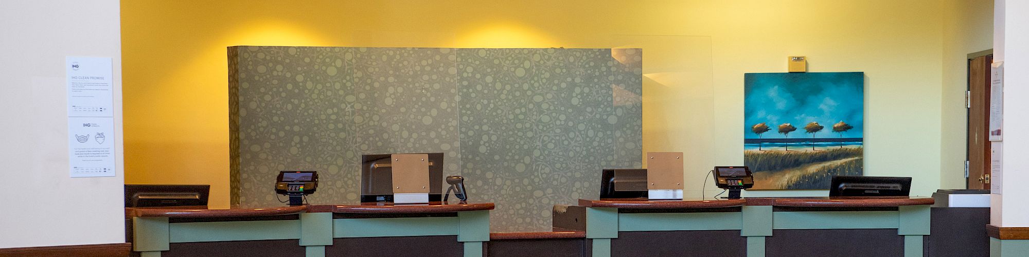 The image shows a reception desk in a lobby area, with chairs and a table in the foreground. A plant is on the table, completing the scene.