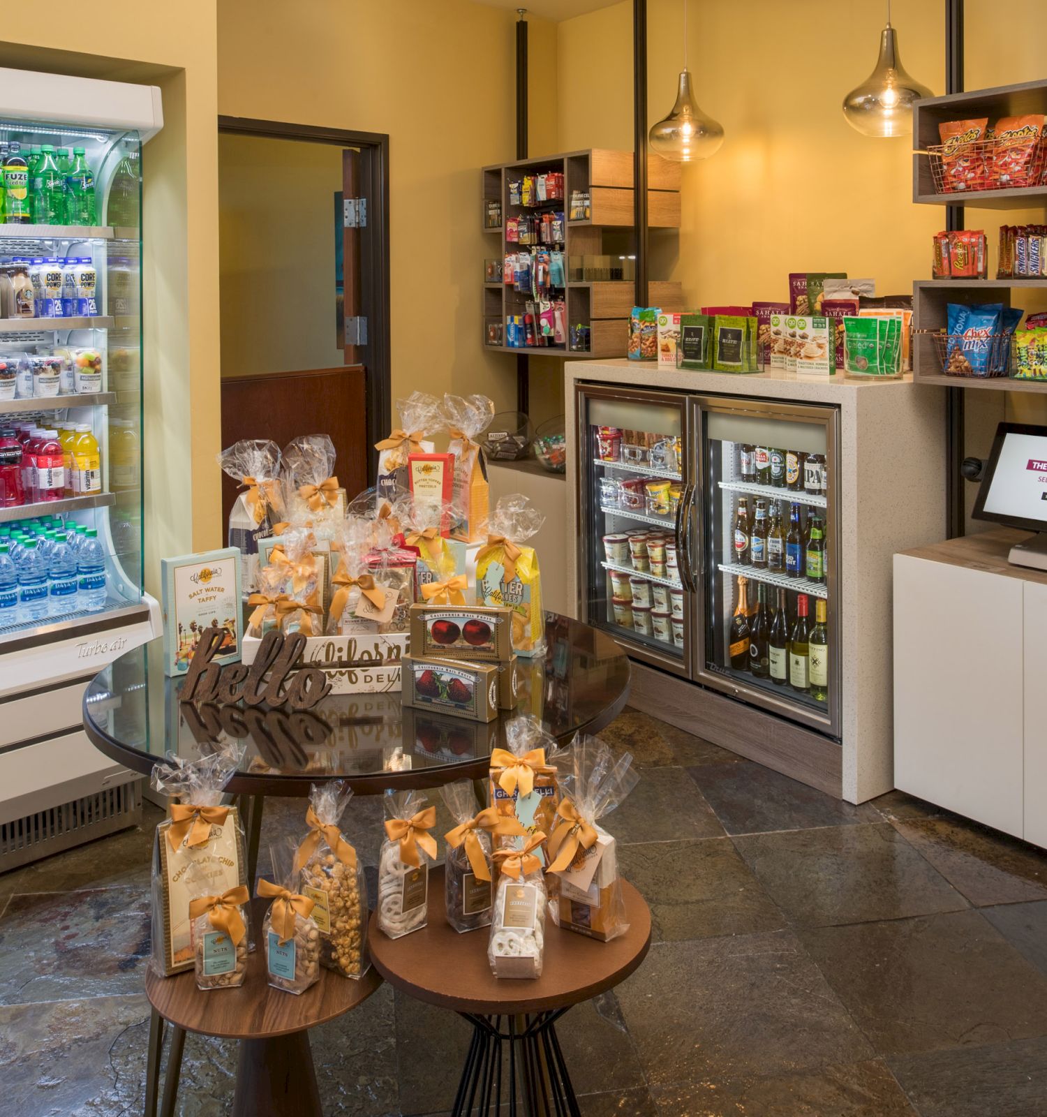 The image shows a well-organized snack area with a refrigerated section, shelves of snacks and candy, a computer on a counter, and displays of packaged treats.