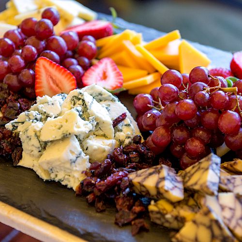 The image features a platter with assorted cheeses, grapes, strawberries, and dried fruits arranged on a slate board.