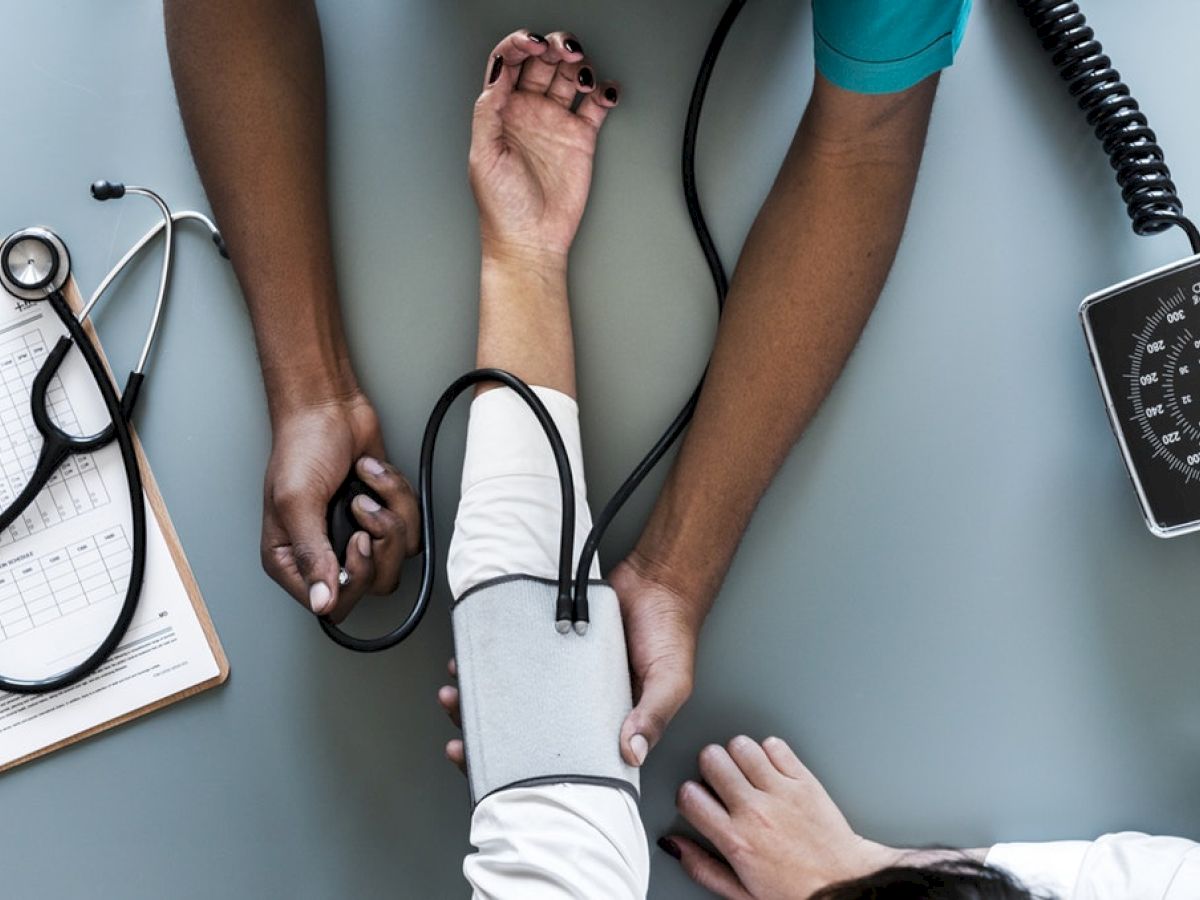 A healthcare professional is measuring a patient's blood pressure using a sphygmomanometer. A stethoscope and clipboard are also present on the table.