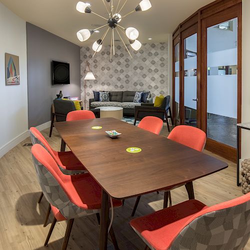 This image shows a modern conference room with a long table, colorful chairs, a couch, artwork on the walls, and unique lighting fixtures.