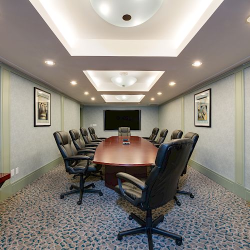 A modern conference room with a long table, leather chairs, a large screen at the end, and framed pictures on the walls.