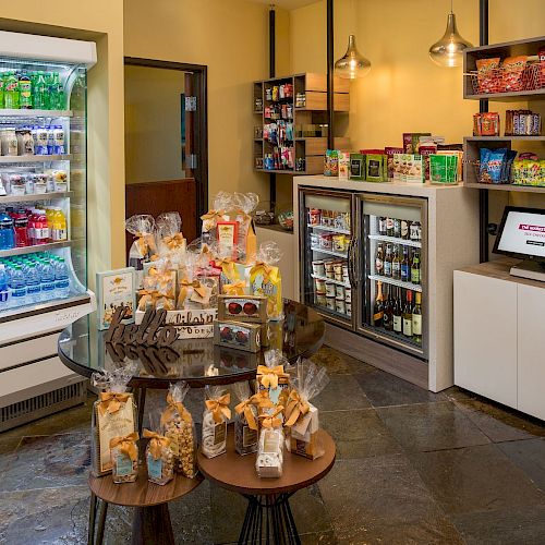 The image shows a small convenience store with a variety of drinks, snacks, and a checkout counter with a computer terminal.