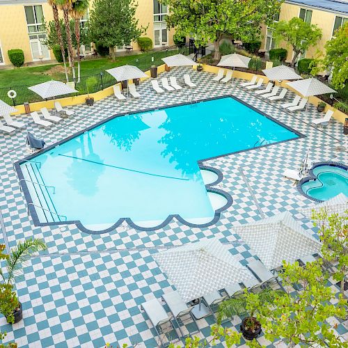 An outdoor pool area with lounge chairs, umbrellas, and surrounding trees in a courtyard.