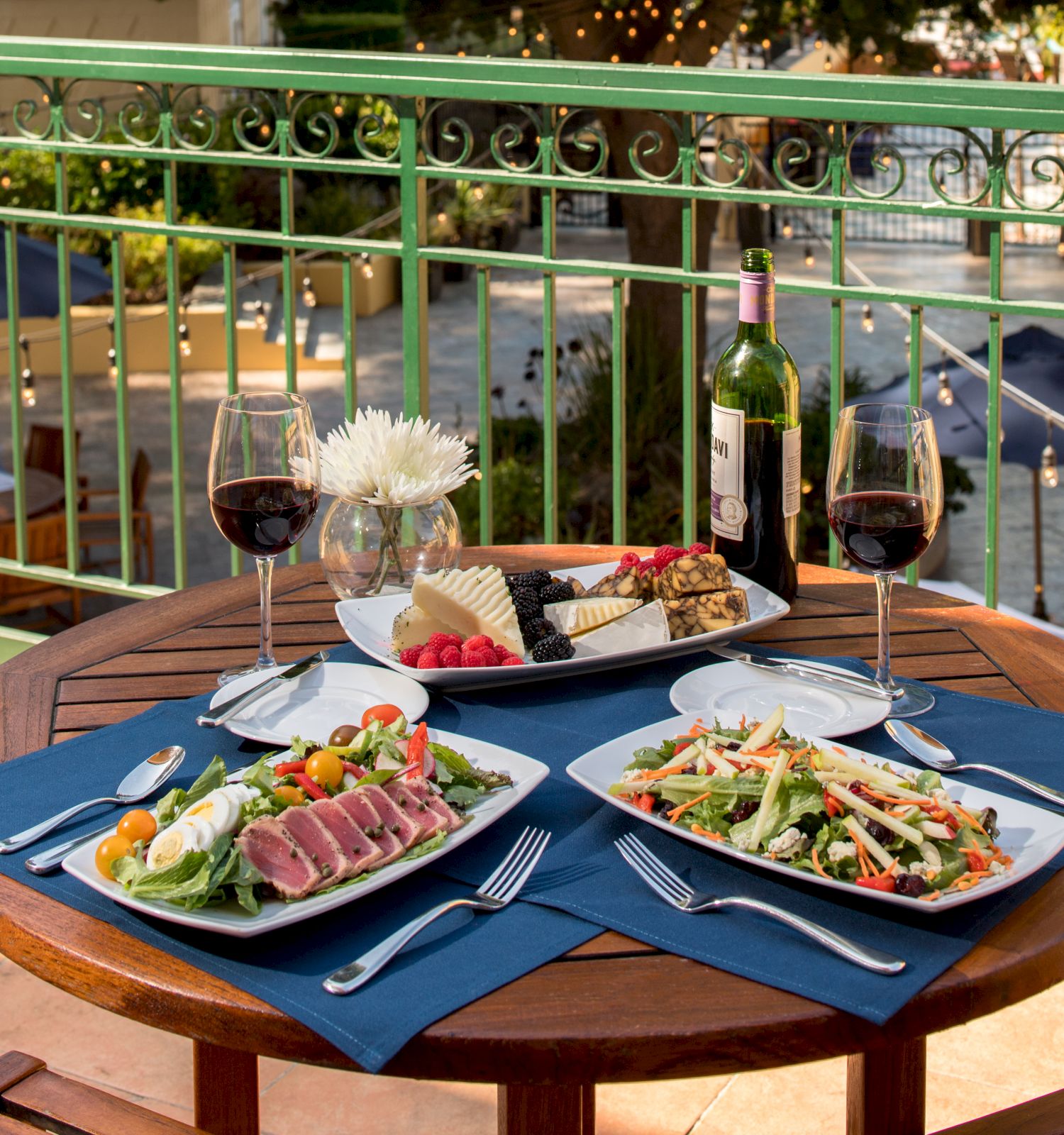 A dining table set for two with salads, wine, cheese, and a scenic view, offering a relaxing ambiance.