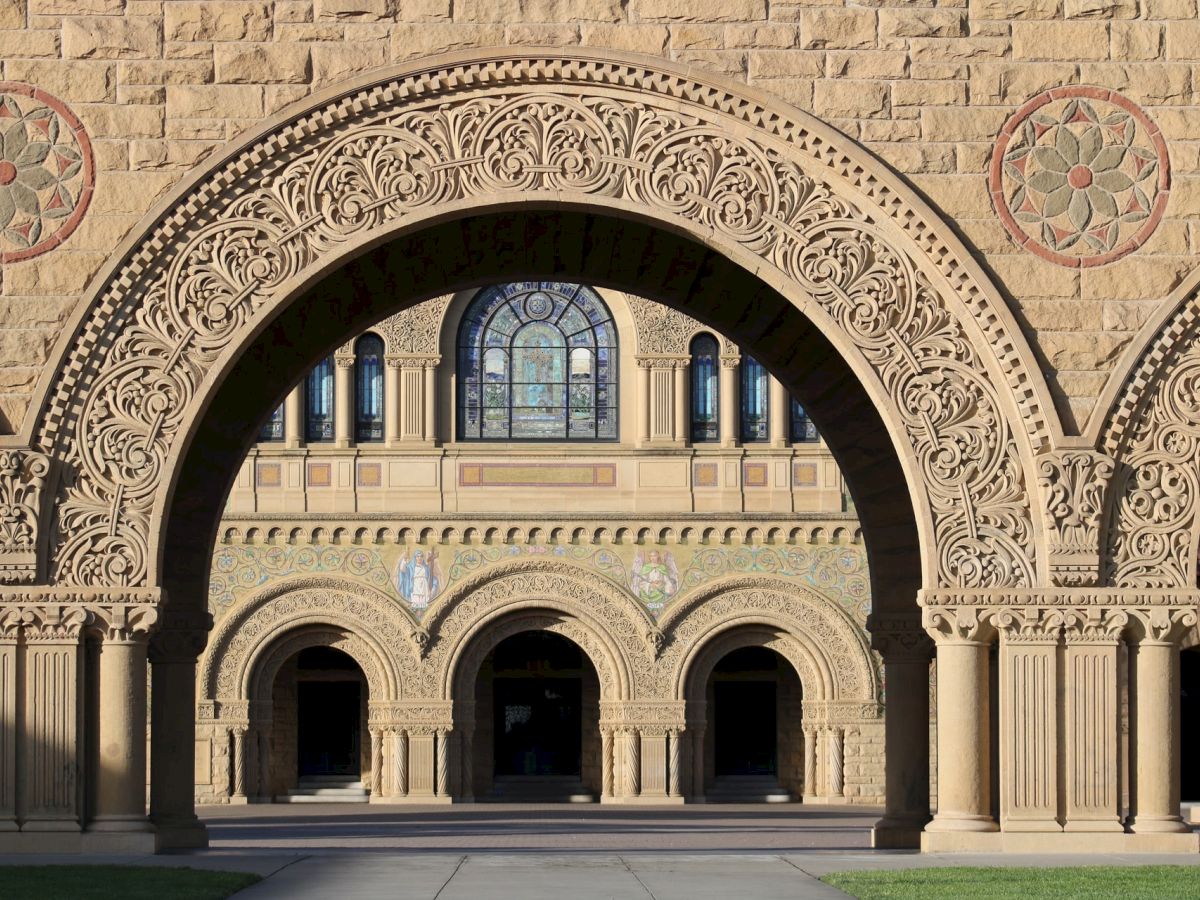 The image depicts a detailed architectural archway with intricate carvings, leading to a building adorned with smaller arches and stained glass windows.