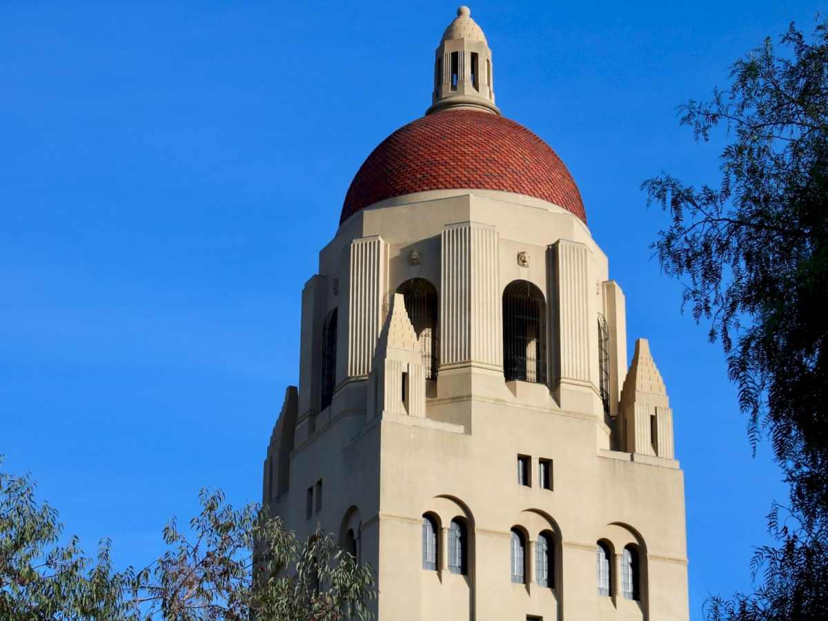 A tall tower with a red-tiled dome stands against a bright blue sky, surrounded by greenery.