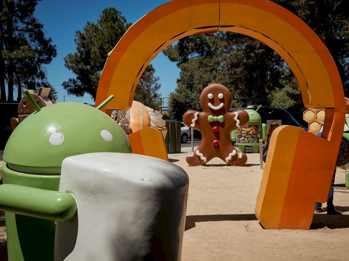 The image shows large statues of Android mascots, including a green robot holding a marshmallow and a gingerbread man, set in an outdoor area.