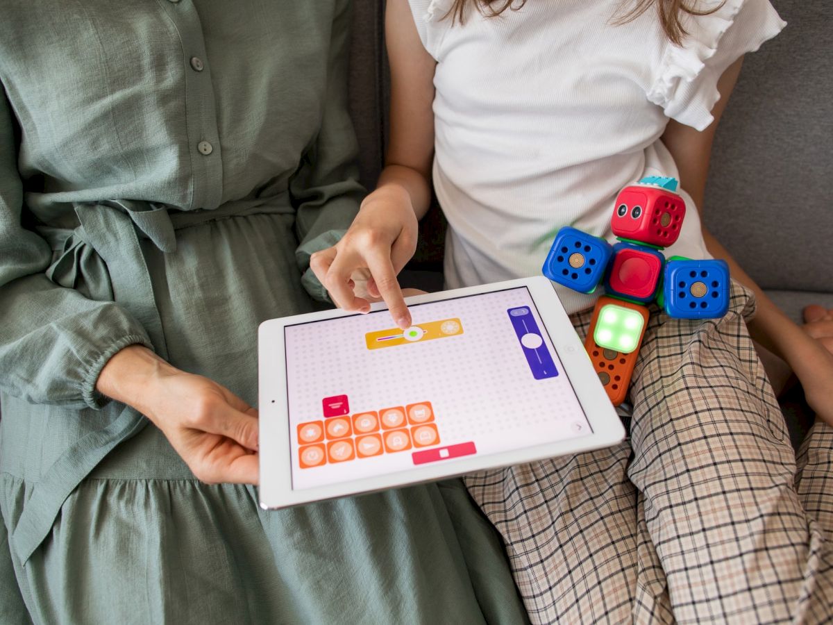 Two people are playing with a tablet and building blocks that have faces, sitting on a sofa.