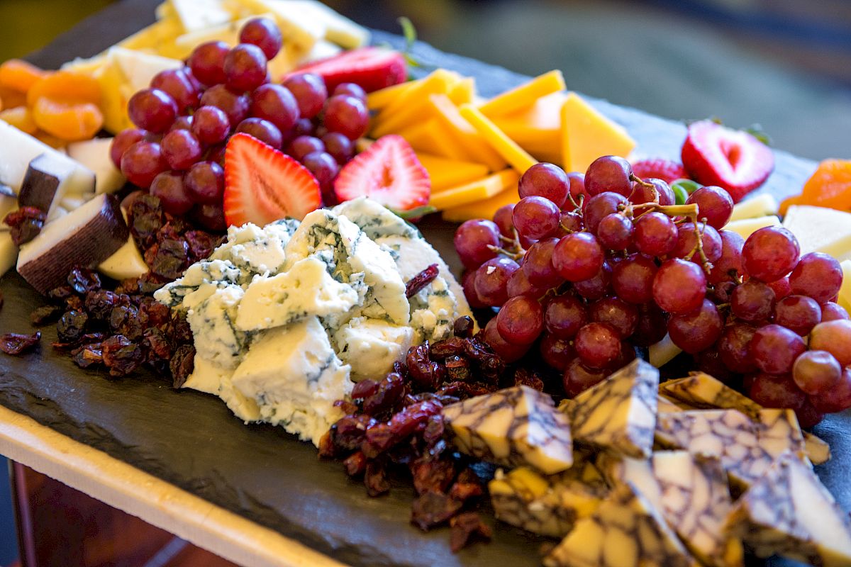A platter with various cheeses, grapes, strawberries, and dried fruits on a slate board. The assortment of different textures makes it visually appealing.