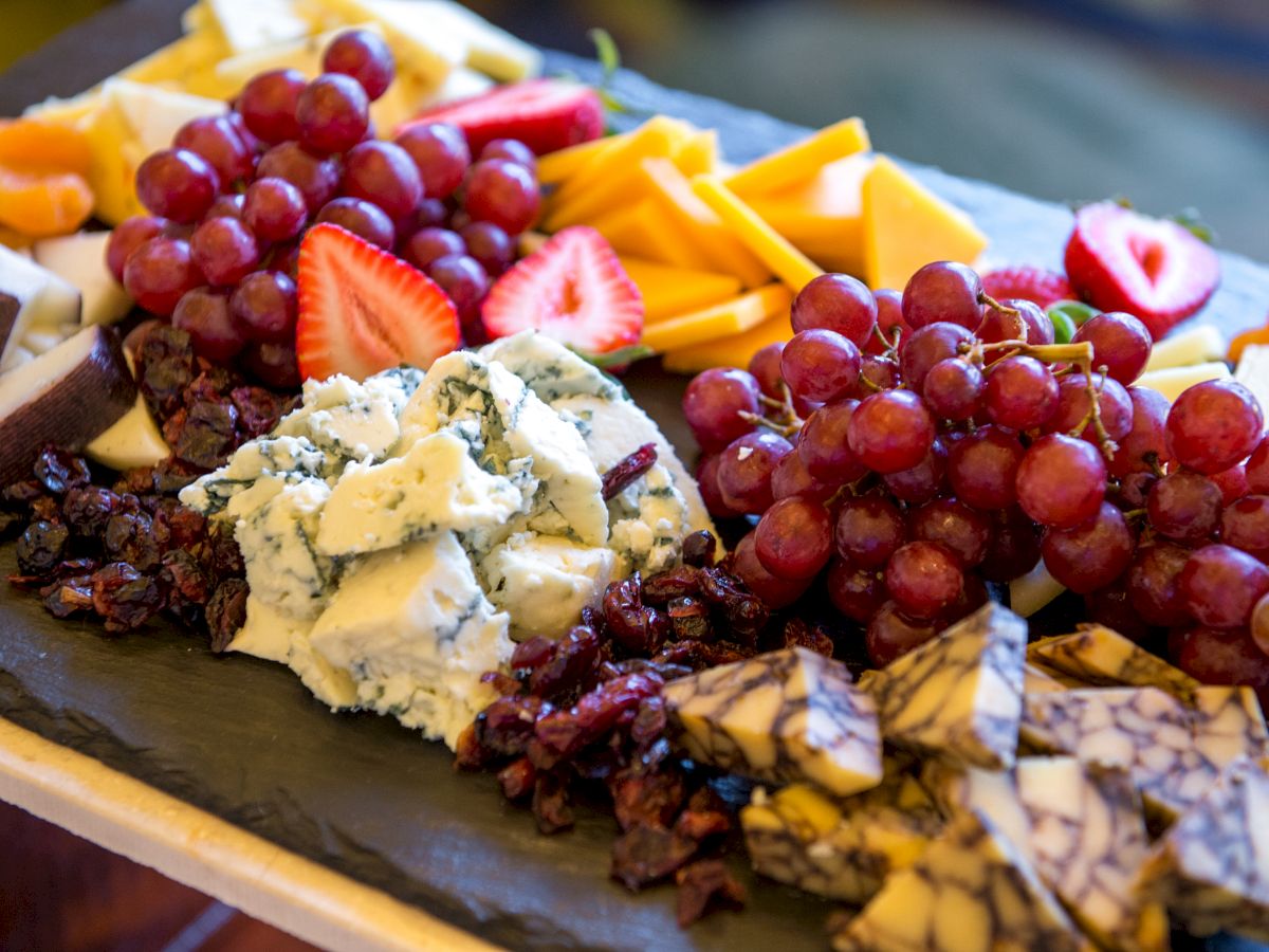 A platter with various cheeses, grapes, strawberries, and dried fruits on a slate board. The assortment of different textures makes it visually appealing.