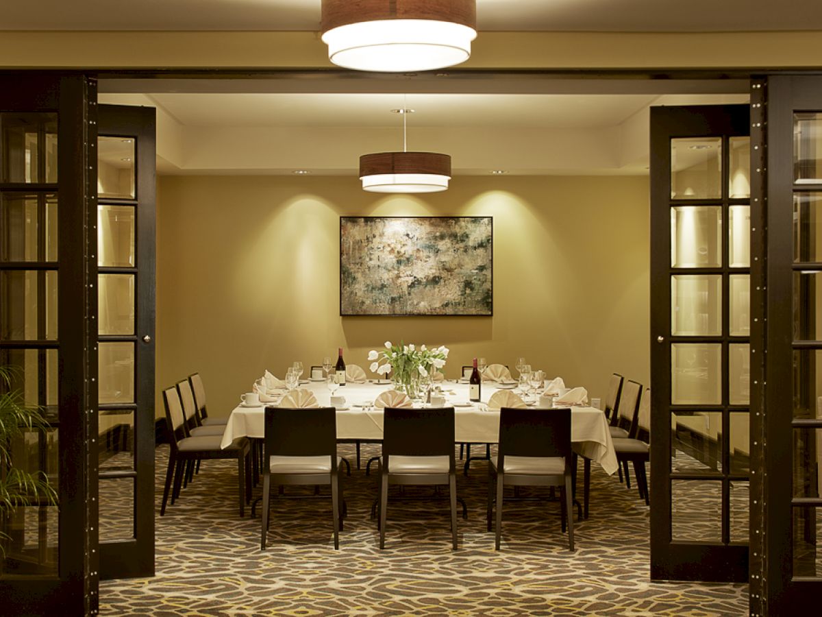 A dining room with a set table, chairs, paintings on the wall, and warm lighting, viewed through open glass-paneled doors ending the sentence.