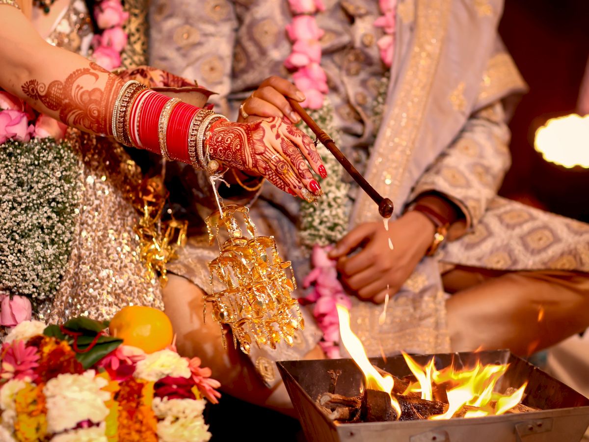 A couple partakes in a traditional wedding ceremony with intricate outfits, floral garlands, and a ceremonial fire.