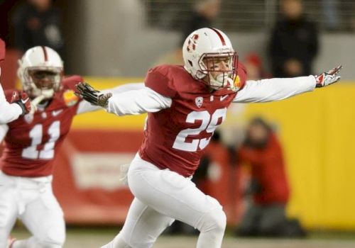 Two football players in red and white uniforms are celebrating on the field. One player has arms outstretched, and the other is in the background.