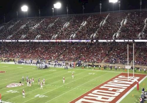 A football game is being played in a stadium at night with a large crowd present. The end zone shows "Stanford" written on the turf.