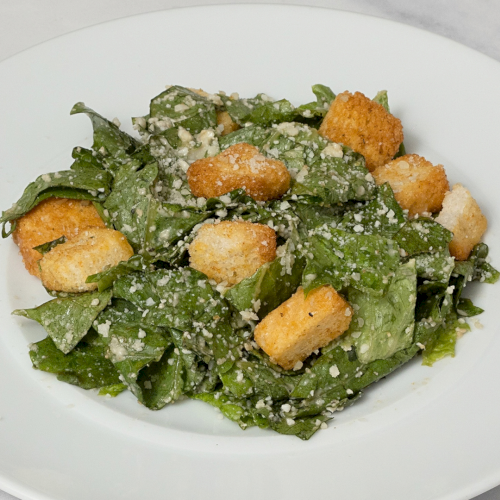 A Caesar salad on a white plate, topped with croutons and grated Parmesan over chopped romaine.