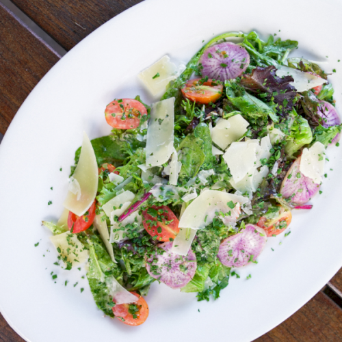 A fresh salad with mixed greens, cherry tomatoes, cucumbers, feta, olives, and herbs tossed in a light vinaigrette.
