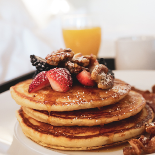 A stack of fluffy pancakes topped with berries and a drizzle of syrup, with a glass of orange juice in the background.