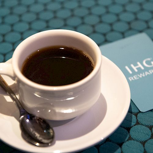 A cup of coffee on a saucer beside a blue notebook, with a pen resting on the page.